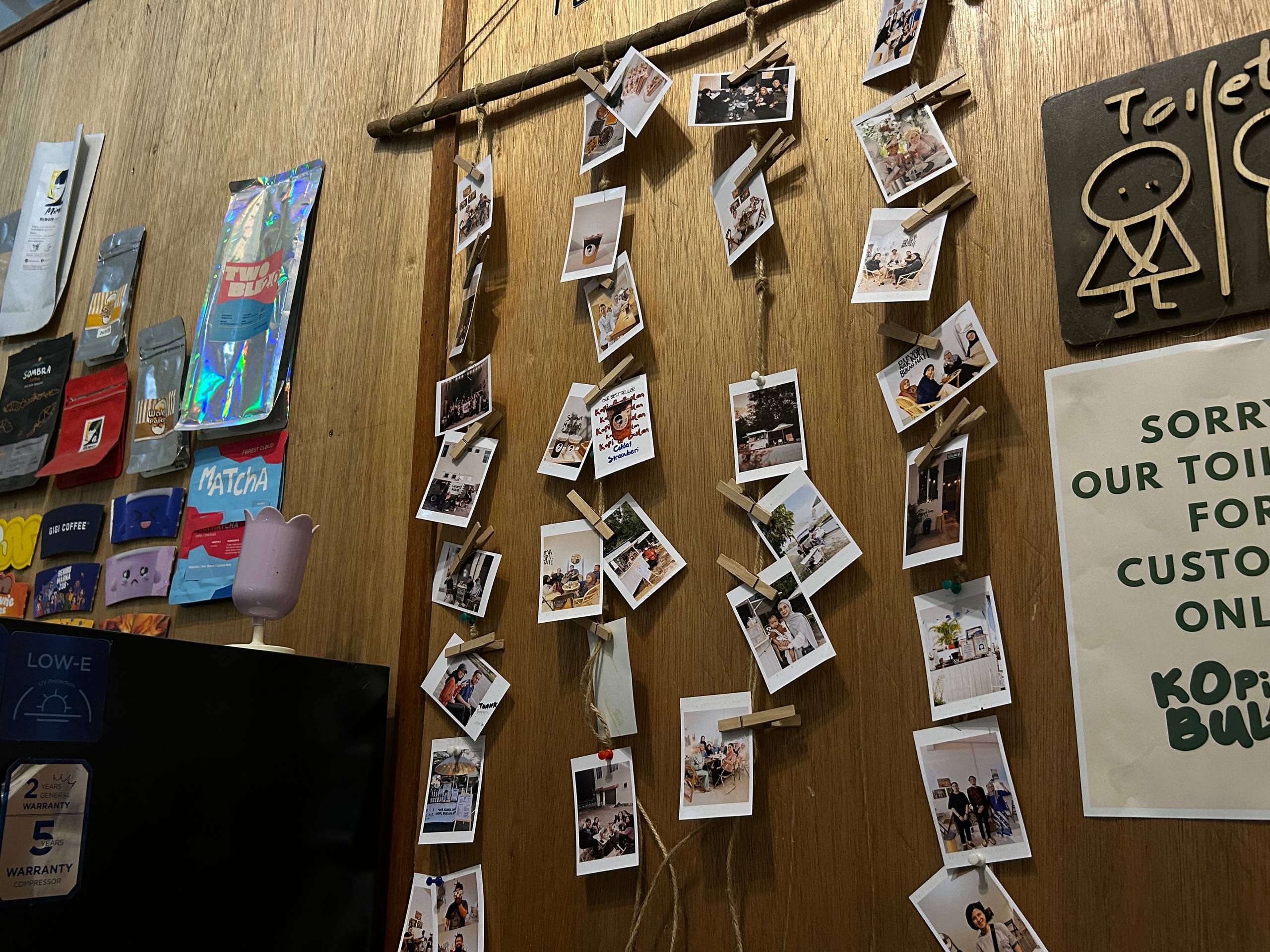 Customer photographs clipped along strings on the wooden Kopi & Bulan memory wall.